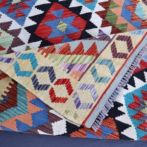 May include: A colorful woven rug with a geometric pattern in shades of red, blue, green, and yellow. The rug has a fringed edge and is folded in half.