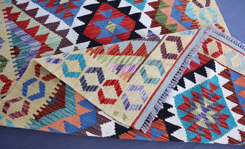 May include: A colorful woven rug with a geometric pattern in shades of red, blue, green, and yellow. The rug has a fringed edge and is folded in half.
