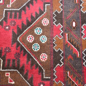 Puede incluir: Primer plano de una alfombra roja, marr&oacute;n y negra con un patr&oacute;n geom&eacute;trico. La alfombra tiene un borde blanco y presenta un dise&ntilde;o repetitivo de flores y diamantes.