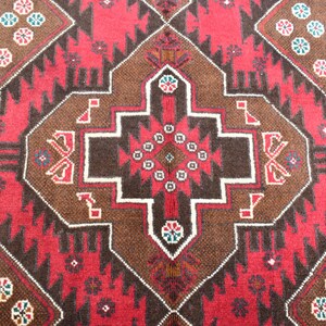 Puede incluir: Un primer plano de una alfombra roja, marr&oacute;n y blanca con intrincados dise&ntilde;os geom&eacute;tricos. La alfombra tiene un estilo persa tradicional.