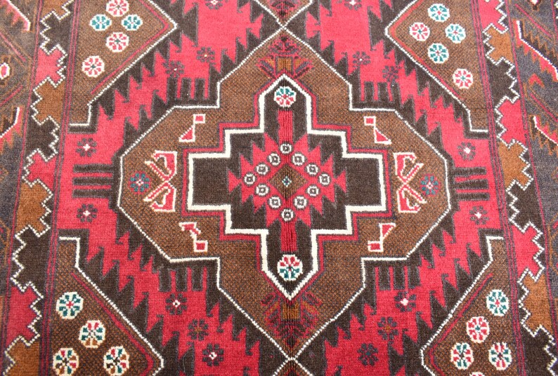 Puede incluir: Un primer plano de una alfombra roja, marr&oacute;n y blanca con intrincados dise&ntilde;os geom&eacute;tricos. La alfombra tiene un estilo persa tradicional.