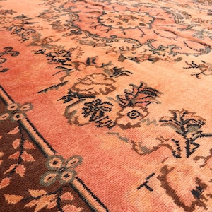 May include: A large, rectangular rug with an intricate floral pattern. The rug features a warm color palette of peach, brown, and black. The border is a darker shade of brown, and the central design showcases detailed floral motifs.