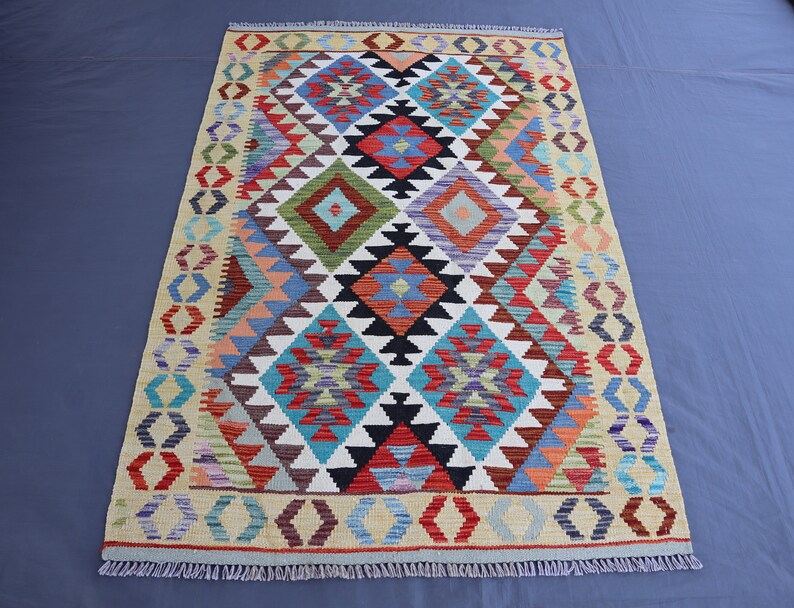 May include: A colorful rug with a geometric pattern in shades of red, blue, green, and white. The rug has a fringe border.