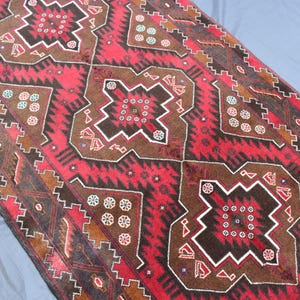 Puede incluir: Una alfombra roja, marr&oacute;n y blanca con un dise&ntilde;o geom&eacute;trico. La alfombra tiene un aspecto tradicional y est&aacute; hecha de lana.