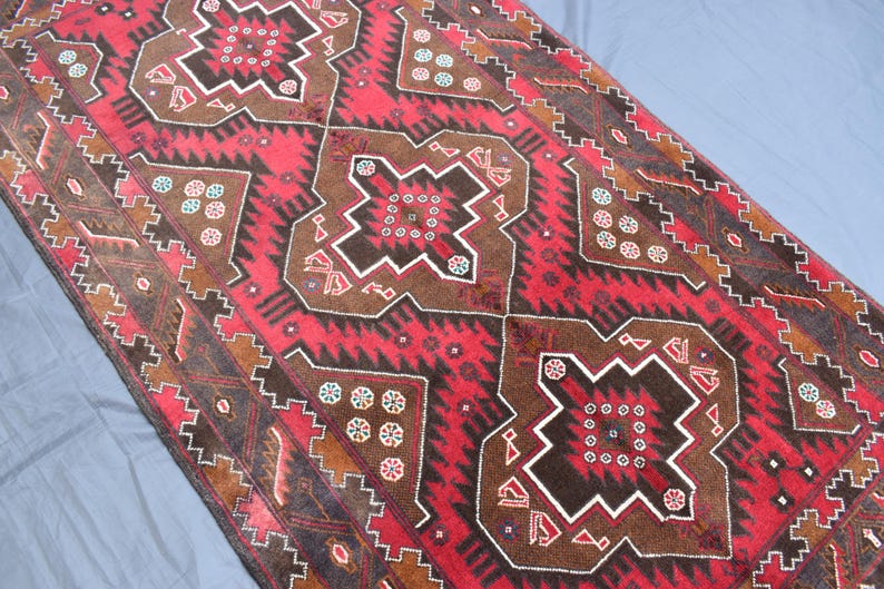 Puede incluir: Una alfombra roja, marr&oacute;n y blanca con un dise&ntilde;o geom&eacute;trico. La alfombra tiene un aspecto tradicional y est&aacute; hecha de lana.
