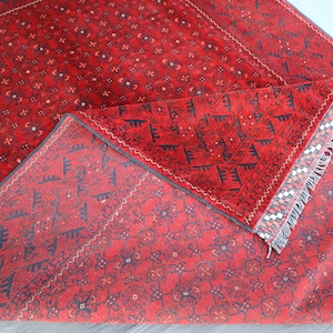 May include: A red rug with a geometric pattern and fringe. The rug is folded in half, showing the back side of the rug.