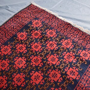 May include: A red and blue rug with a geometric pattern. The rug has a fringe border.
