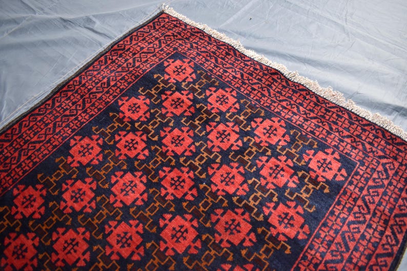 May include: A red and blue rug with a geometric pattern. The rug has a fringe border.