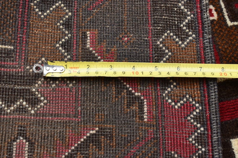 Puede incluir: Primer plano de una alfombra con estampado marr&oacute;n, rojo y blanco con una cinta m&eacute;trica amarilla en el borde inferior. La cinta indica "16FFFT 2 3 4 5 6 7 8 9 10 1 2 3 4 5 6 7 8 9 20 1".