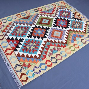 May include: A colorful rug with a geometric pattern in shades of red, blue, green, orange, and white. The rug has a fringe border.