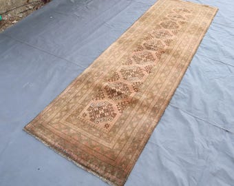 Puede incluir: Una alfombra de corredor rectangular de estilo vintage con un patrón geométrico central en tonos marrón, beige y melocotón. La alfombra tiene un borde con flecos y un borde con un diseño repetido. La alfombra está colocada sobre una superficie gris.