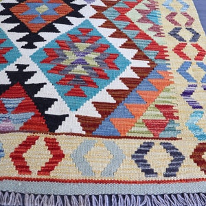 May include: A colorful rug with a geometric pattern in shades of red, blue, green, and yellow. The rug has a fringe border.