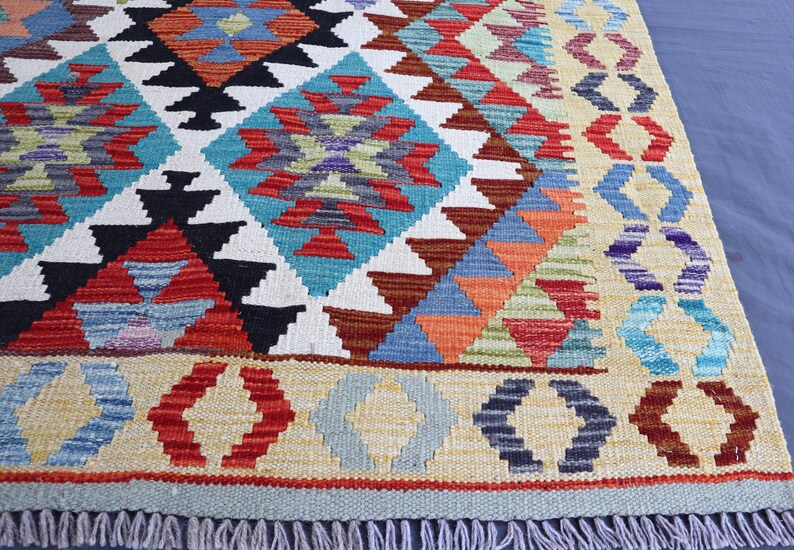 May include: A colorful rug with a geometric pattern in shades of red, blue, green, and yellow. The rug has a fringe border.