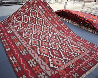 May include: A red, white, and brown patterned rug with a geometric design. The rug is folded in half and is lying on a blue surface.