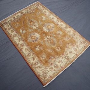 Könnte beinhalten: Draufsicht auf einen rechteckigen Teppich mit aufwendigem Blumenmuster. Der Teppich hat ein warmes, goldbraunes Mittelfeld mit cremefarbenen Bordüren. Das Design umfasst Blumenmotive in Lila-, Rot- und Grüntönen.