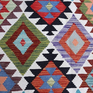 May include: A colorful rug with a geometric pattern in shades of red, blue, green, and white. The rug is woven with a traditional design and has a textured surface.