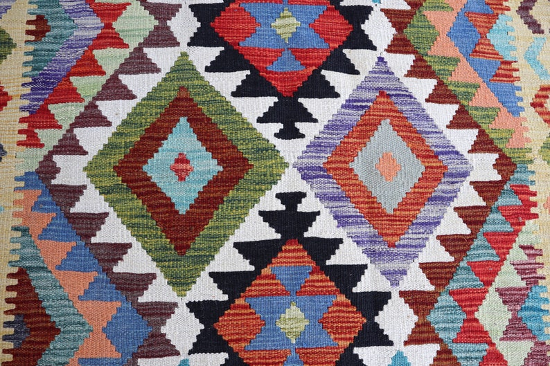 May include: A colorful rug with a geometric pattern in shades of red, blue, green, and white. The rug is woven with a traditional design and has a textured surface.