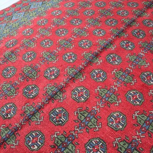 Op de afbeelding: Rood tapijt met een herhalend patroon van blauwe, groene en witte geometrische vormen.