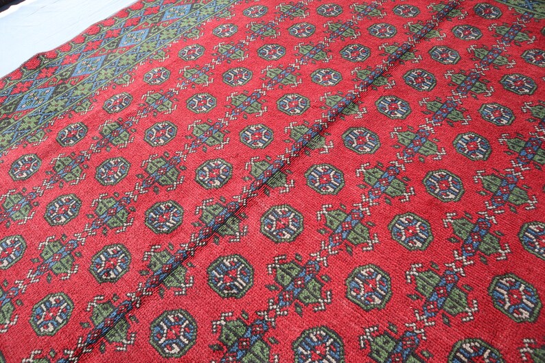 Op de afbeelding: Rood tapijt met een herhalend patroon van blauwe, groene en witte geometrische vormen.