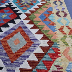 May include: A colorful rug with a geometric pattern in shades of red, blue, green, and white. The rug has a fringe border and is made of wool.