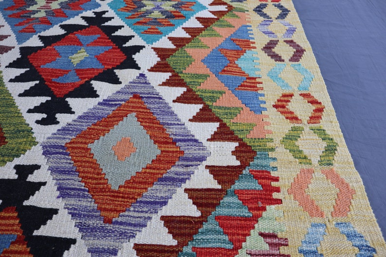 May include: A colorful rug with a geometric pattern in shades of red, blue, green, and white. The rug has a fringe border and is made of wool.