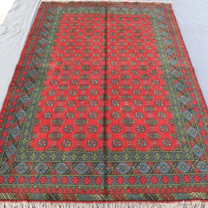 Op de afbeelding: Een rood, blauw en groen gestreept tapijt met een franje rand. Het tapijt heeft een traditioneel ontwerp met herhalende geometrische vormen.