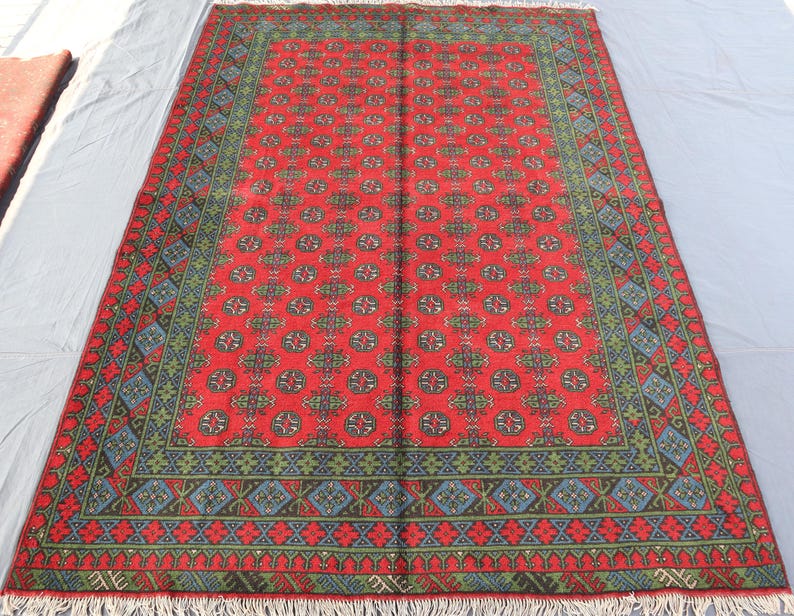 Op de afbeelding: Een rood, blauw en groen gestreept tapijt met een franje rand. Het tapijt heeft een traditioneel ontwerp met herhalende geometrische vormen.