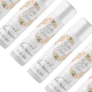 May include: Five white lip balm tubes with floral designs and the text "Baby in Bloom" and "Sarah's Baby Shower" with the date "12.02.2023".