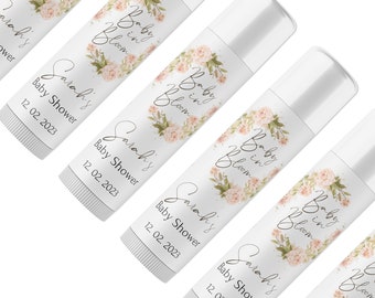 May include: Five white lip balm tubes with floral designs and the text "Baby in Bloom" and "Sarah's Baby Shower" with the date "12.02.2023".