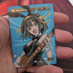 May include: A custom-painted trading card featuring an anime-style character with bunny ears playing a guitar. The card has a blue background with the text "Ms. Bumblefl" and "1/5". The character is wearing a black outfit and has a bow tie.