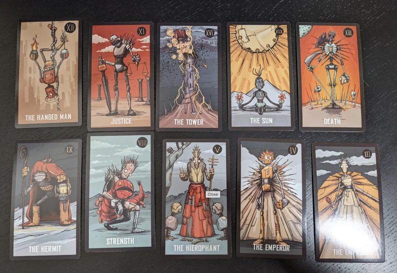 May include: A collection of ten tarot cards featuring stylized illustrations. Each card has a unique design and title, including "The Hanged Man," "Justice," "The Tower," and "The Sun." The cards have a dark border and a muted color palette.