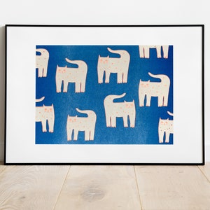 Op de afbeelding: Een ingelijst print met een blauwe achtergrond en een herhalend patroon van witte katten met roze neuzen en ogen. De katten staan in verschillende poses, sommige staan, sommige zitten en sommige liggen.