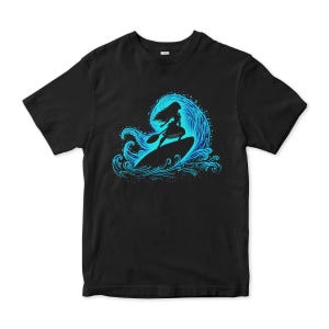 Puede incluir: Camiseta negra con un dise&ntilde;o azul de una persona surfeando una ola. El surfista es una silueta, de pie sobre una tabla de surf. La ola est&aacute; detallada con l&iacute;neas arremolinadas y un efecto de salpicadura.