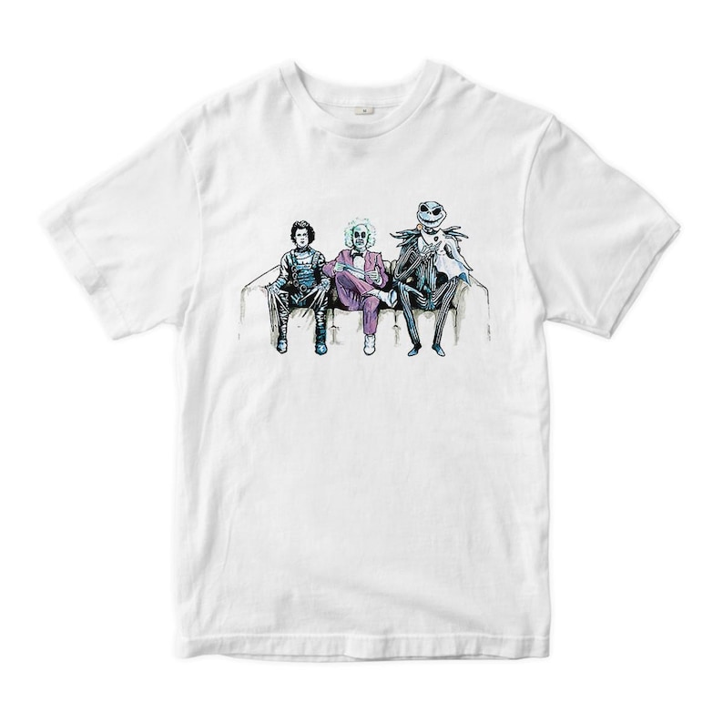 K&ouml;nnte beinhalten: Wei&szlig;es T-Shirt mit einem Grafikdruck von drei Figuren, die auf einer Couch sitzen. Die Figuren sind in verschiedenen Kost&uuml;men gekleidet, darunter ein lila Anzug, ein wei&szlig;er Anzug und ein schwarzer Anzug. Die Figuren stammen aus dem Film "Nightmare Before Christmas".