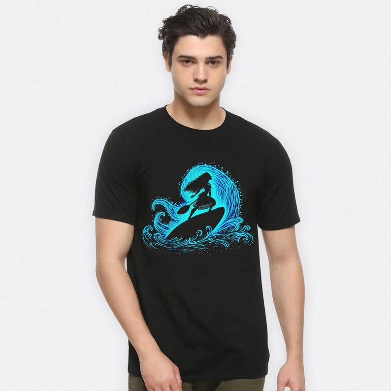 Puede incluir: Camiseta negra con un gr&aacute;fico azul de una persona surfeando una ola. La silueta del surfista se destaca contra una ola, sosteniendo una paleta. El dise&ntilde;o de la ola tiene un efecto degradado, que va del azul oscuro al azul claro.