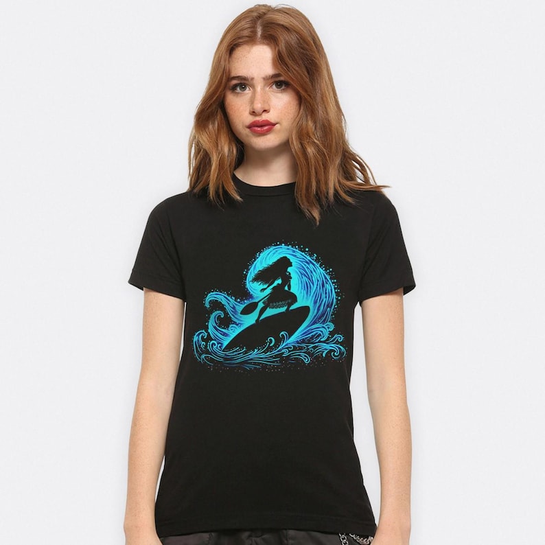 Puede incluir: Camiseta negra con un dise&ntilde;o azul de una persona surfeando una ola. La silueta del surfista se destaca contra una ola azul detallada. El dise&ntilde;o est&aacute; centrado en la camiseta.