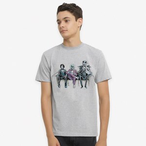 K&ouml;nnte beinhalten: Ein hellgraues T-Shirt mit einem Grafikdruck von drei Figuren aus dem Film Nightmare Before Christmas, die auf einer Couch sitzen. Die Figuren sind Jack Skellington, Sally und Oogie Boogie.