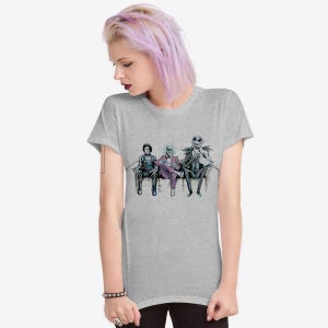 K&ouml;nnte beinhalten: Ein hellgraues T-Shirt mit einem Aufdruck von drei Figuren, die auf einer Couch sitzen. Die Figuren sind in Schwarz, Lila und Gr&uuml;n gekleidet. Die Figuren stammen aus dem Film Nightmare Before Christmas.