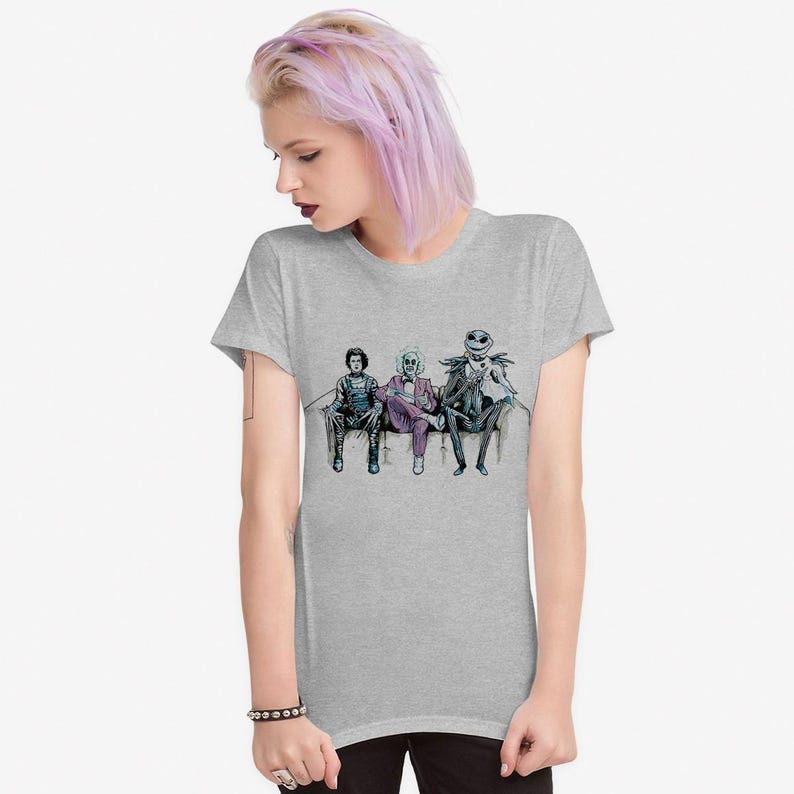 K&ouml;nnte beinhalten: Ein hellgraues T-Shirt mit einem Aufdruck von drei Figuren, die auf einer Couch sitzen. Die Figuren sind in Schwarz, Lila und Gr&uuml;n gekleidet. Die Figuren stammen aus dem Film Nightmare Before Christmas.