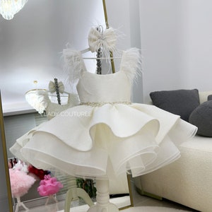 Vestido de gala de tela blanca brillante y detalle de plumas de avestruz.