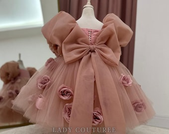Op de afbeelding: Een stoffige roze tule jurk met een grote strik op de rug en 3D-rozenversieringen. De jurk is op een mannequin en heeft de tekst "LADY COUTUREE BY SERAP BADEM" onderaan.