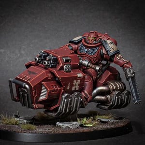 Può includere: Una statuetta in miniatura di una figura rossa corazzata che cavalca un hovercraft rosso. La figura tiene in mano un'arma. L'hovercraft ha più tubi di scarico e un paraurti anteriore. La figura ha un elmetto e un'emblema alato sul petto.