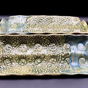 Peut inclure: Deux plateaux de service en céramique faits à la main. Les plateaux rectangulaires présentent une surface texturée et un mélange de couleurs bleu, vert et crème. Les plateaux ont un design unique et organique, idéal pour servir des amuse-gueules.