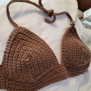 May include: A brown crochet bikini top with adjustable straps. The top features a triangle design and is made of a textured, woven material. The straps are tied at the neck and back.