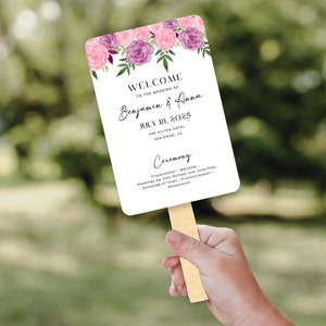 May include: A white wedding ceremony program fan with pink and purple floral illustrations. The text reads "Welcome to the wedding of Benjamin & Anna, July 18, 2025, The Hilton Hotel, San Diego, CA. Ceremony: Processional - Welcome, Readings by John Michael and Julia Pike - Exchange of Vows - Pronouncement - Recessional."