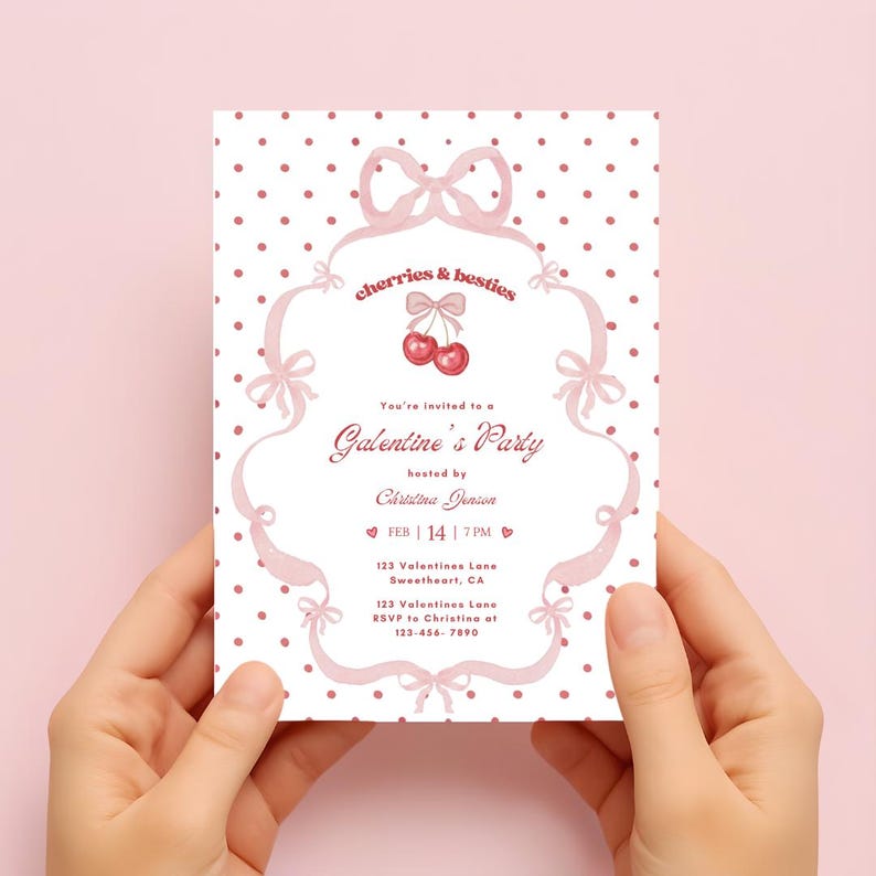 May include: A pink invitation card with the text "cherries & besties" and "Galentine's Party". The card features a bow and cherry design, with the date February 14 and the time 7 PM. The card is held by two hands.