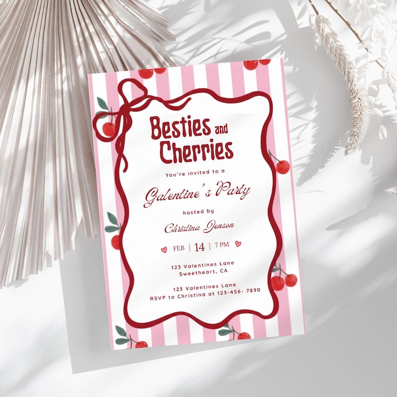以下が含まれることがあります： 「Besties and Cherries」と「Galentine's Party」の文字が入った、ピンクと白のストライプの招待状。招待状には日付、時間、場所が記載されています。赤いさくらんぼと装飾的なボーダーがデザインを完成させています。