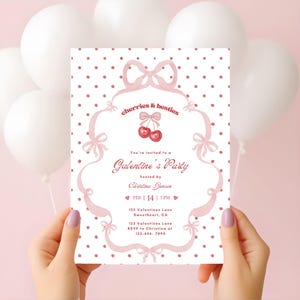 May include: A Galentine's Party invitation with a pink and white polka dot background. The invitation features pink bows and the text "cherries & besties". The invitation is held by a person with manicured nails.
