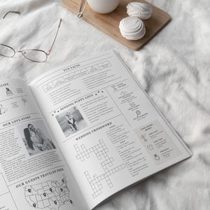 May include: An open wedding journal with text and photos, featuring a crossword puzzle, fun facts, and a map of guest locations. A wooden cutting board with a white mug and two meringues is in the background.