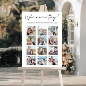 May include: A white sign on a wooden easel with the text "Where were they?" in elegant script. The sign features 12 small photos, likely for a game at a wedding or engagement party. The text below asks, "Can you figure out where the future bride and groom are in every picture?"